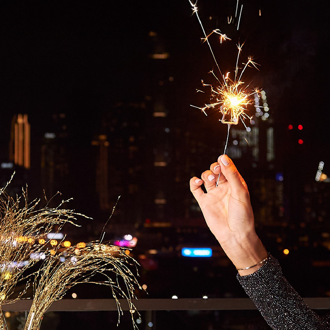 Hand holding a lit sparkler against a city skyline at night